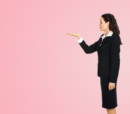 Full body profile side of beautiful businesswoman showing something or copy spase for product. Brunette woman looking at her hand in business studio concept, isolated on rose pink yellow background.の写真素材