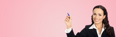 Happy smiling cheerful beautiful young business woman writing or drawing something on screen or transparent glass, by blue marker, isolated over rose pink backgroundの写真素材