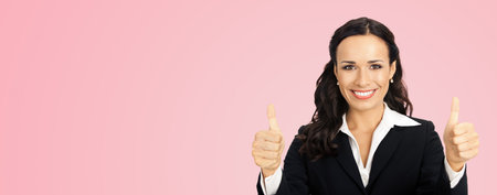 Businesswoman in black confident suit showing thumbs up gesture, over rose pink color background. Happy smiling gesturing brunette woman at studio. Business concept photo.の写真素材