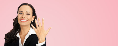 Businesswoman in black confident suit showing five fingers, over rose pink color background. Happy smiling gesturing brunette woman at studio. Business success concept.の写真素材