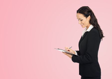 Happy smiling young beautiful business woman with clipboard writing, isolated over rose pink backgroundの写真素材
