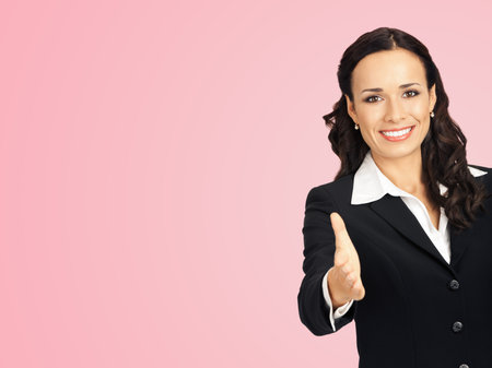 Happy smiling young beautiful business woman in black confident suit and white blouse, giving hand for handshake, isolated over rose pink color background with copy space.の写真素材