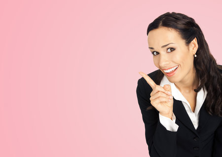 Happy smiling executive woman in black confident suit, pointing showing copy space. Business concept. Rose pink colour background. Brunette businesswoman. Wide image.の写真素材