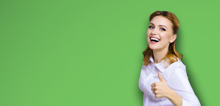 Excited happy smiling businesswoman, showing thumb finger up or like hand sign gesture. Success in business studio concept. Isolated on bright green background.の写真素材