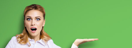 Portrait of very happy, excited surprised, astonished businesswoman with wide opened eyes, mouth, showing copy space text area. Success in business concept. Bright green background.の写真素材