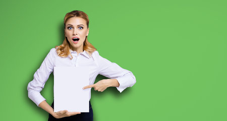 Very happy, excited surprised, astonished businesswoman with wide opened eyes, mouth, showing blank paper signboard. Success in business concept. Copy space place for text. Bright green background.の写真素材
