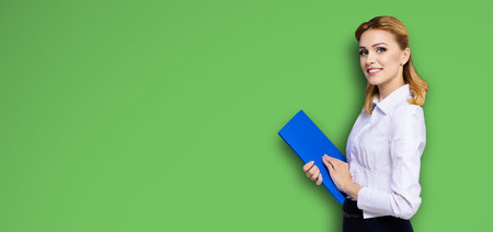 Happy smiling businesswoman, with copy space area for some slogan or text. Confident blond woman in white shirt with blue folder, bright green color background. Business concept.の写真素材