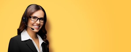 Contact Call Center Service. Customer support, sales agent. Caller answering phone operator or businesswoman in headset. Face portrait of woman in glasses spectacles. Yellow background. Copy space.の写真素材