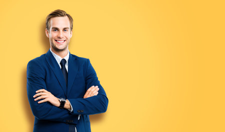 Portrait of businessman in blue suit and tie, with crossed arms, isolated over vivid yellow colour background. Business concept. Smiling man at studio picture. Copy space for some text.の写真素材