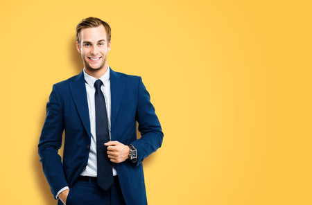 Portrait of happy confident businessman in blue suit and tie, isolated over vivid yellow colour background. Business success concept. Smiling man at studio picture. Copy space for ad text or slogan.の写真素材