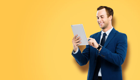Portrait of smiling businessman using touchpad tablet pc, over vivid yellow colour background. Success in business concept studio picture. Copy space for ad text.の写真素材