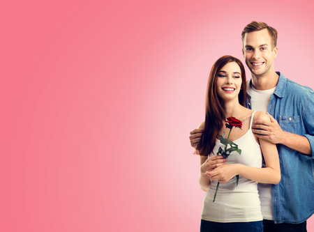 Love, relationship, dating, flirting, romantic concept - portrait of young happy smiling hugging couple with flower, close to each other, isolated on vivid rose pink background.の写真素材