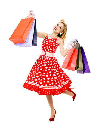 Full body of jumping, running, dancing woman in pinup red dress holding, showing carrying shopping bags, isolated over white background. Sales discounts rebates or consumer bank credit ad conceptの写真素材