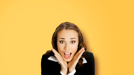 Excited surprised, shocked, astonished businesswoman. Business woman with open mouth, hands near face, on yellow background.の写真素材