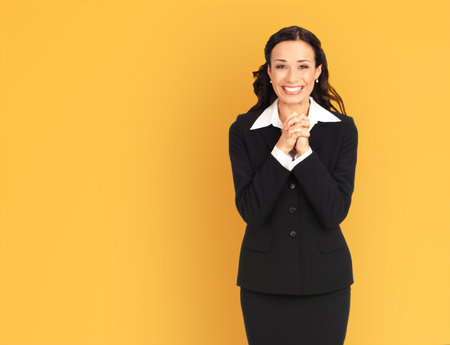 Portrait image - excited smiling positive businesswoman wear black confident suit, isolated against yellow background. Happy gesturing, praying hope for good luck woman. Business success ad concept.の写真素材