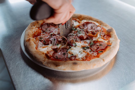 Closeup hand of chef baker in white uniform cutting pizza at kitchen