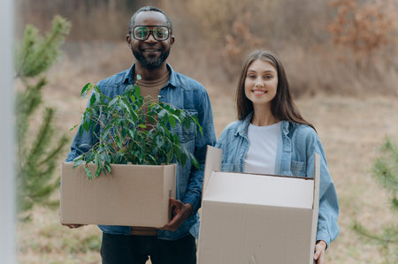 A happy young family is moving into a house. A black man and woman are holding cardboard boxes for moving, smiling. moving boxesの写真素材