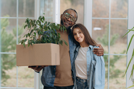 A happy young family is moving into a house. A black man and woman are holding cardboard boxes for moving, smiling. moving boxesの写真素材