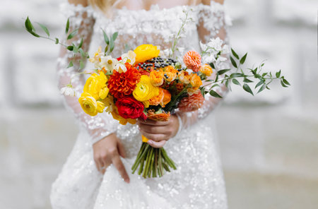 bride in white wedding dress holding a bouquet of bright flowers. a bouquet of yellow, red and orange flowersの写真素材