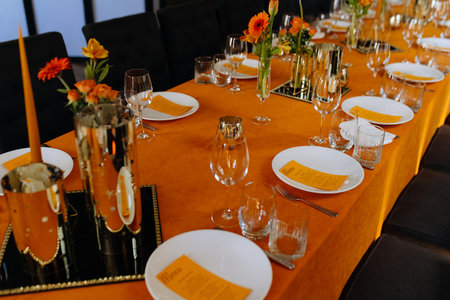 Cutlery, napkins, plates, flowers on an orange table. Table setting. Orange table decor. birthday celebration, wedding in a restaurantの写真素材