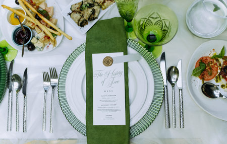 Wedding banquet. Table with green decor for guests, served with cutlery, green flowers and dishes,...