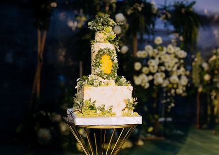 wedding cake in the evening. evening ceremony. an Elegant tiered wedding cake illuminated with romantic lights, set against a floral outdoor backdropの写真素材