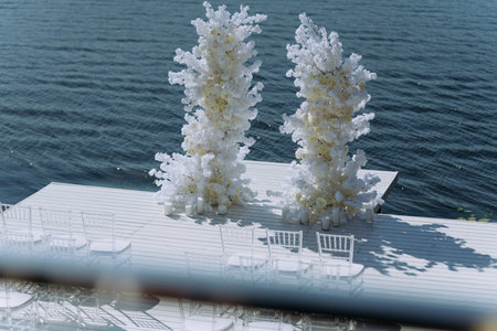 A beautiful floral arch for wedding ceremonies and white chairs for guests. wedding ceremony with a beautiful decor in the form of an arch for the bride and groom against the background of the river.の写真素材