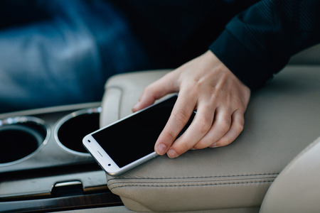 in car mobile phone in hand on beige leather armrest in the carの写真素材