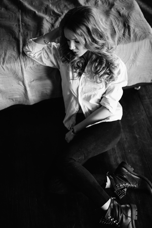 A girl with long blond hair dressed in black jeans, a striped shirt and black shoes sitting on the bed with blue linens. Fashionable casual outfit.の写真素材