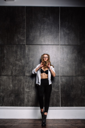 Fashion style of fashion. Fashionable woman in stylish clothes posing on a gray background in the studio. A beautiful sexy girl wearing black glasses, black jeans, black shoes, a white striped shirt.の写真素材