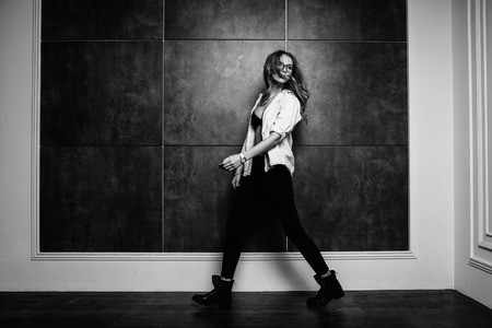 Fashion style of fashion. Fashionable woman in stylish clothes posing on a gray background in the studio. A beautiful sexy girl wearing black glasses, black jeans, black shoes, a white striped shirt.の写真素材