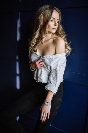 Young beautiful woman model in a white shirt, black jeans, confident, blue backgroundの写真素材