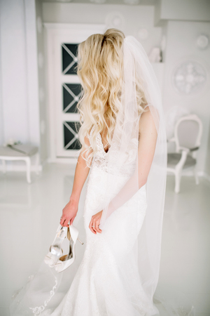 Wedding. Bride in a beautiful dress indoors in a white studio, like at home. The fashionable wedding style is taken in full length. Young attractive blond model with curly hair, like a brideの写真素材