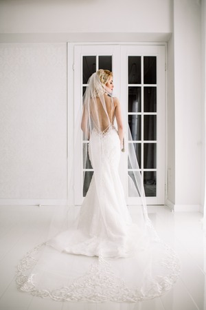 Wedding. Bride in a beautiful dress indoors in a white studio, like at home. The fashionable wedding style is taken in full length. Young attractive blond model with curly hair, like a brideの写真素材