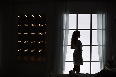 Silhouette of a fashion woman by the window. Wonderful portrait of a girl in a beautiful silk dressing gown.の写真素材