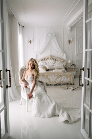 Wedding. Bride in a beautiful dress indoors in a white studio, like at home. The fashionable wedding style is taken in full length. Young attractive blond model with curly hair, like a brideの写真素材