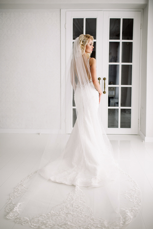 Wedding. Bride in a beautiful dress indoors in a white studio, like at home. The fashionable wedding style is taken in full length. Young attractive blond model with curly hair, like a brideの写真素材