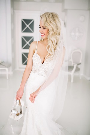 Wedding. Bride in a beautiful dress indoors in a white studio, like at home. The fashionable wedding style is taken in full length. Young attractive blond model with curly hair, like a brideの写真素材
