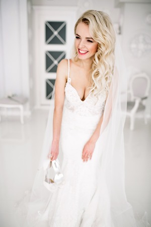 Wedding. Bride in a beautiful dress indoors in a white studio, like at home. The fashionable wedding style is taken in full length. Young attractive blond model with curly hair, like a brideの写真素材