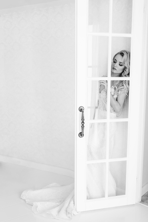 Wedding. Bride in a beautiful dress indoors in a white studio, like at home. The fashionable wedding style is taken in full length. Young attractive blond model with curly hair, like a brideの写真素材