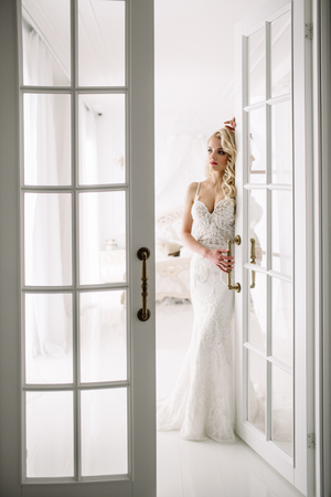Wedding. Bride in a beautiful dress indoors in a white studio, like at home. The fashionable wedding style is taken in full length. Young attractive blond model with curly hair, like a brideの写真素材