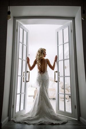 Wedding. Bride in a beautiful dress indoors in a white studio, like at home. The fashionable wedding style is taken in full length. Young attractive blond model with curly hair, like a brideの写真素材