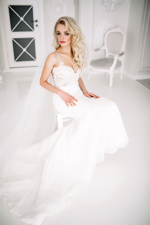 Wedding. Bride in a beautiful dress indoors in a white studio, like at home. The fashionable wedding style is taken in full length. Young attractive blond model with curly hair, like a brideの写真素材