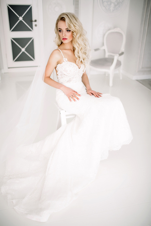 Wedding. Bride in a beautiful dress indoors in a white studio, like at home. The fashionable wedding style is taken in full length. Young attractive blond model with curly hair, like a brideの写真素材