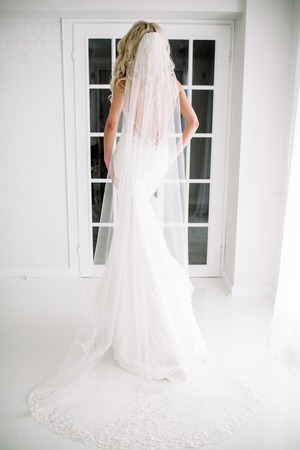 Wedding. Bride in a beautiful dress indoors in a white studio, like at home. The fashionable wedding style is taken in full length. Young attractive blond model with curly hair, like a brideの写真素材