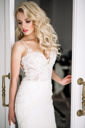 Wedding. Bride in a beautiful dress indoors in a white studio, like at home. The fashionable wedding style is taken in full length. Young attractive blond model with curly hair, like a brideの写真素材