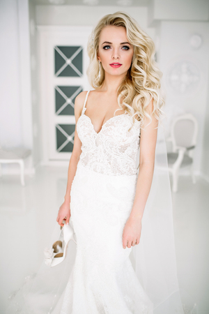 Wedding. Bride in a beautiful dress indoors in a white studio, like at home. The fashionable wedding style is taken in full length. Young attractive blond model with curly hair, like a brideの写真素材