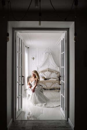Wedding. Bride in a beautiful dress indoors in a white studio, like at home. The fashionable wedding style is taken in full length. Young attractive blond model with curly hair, like a brideの写真素材