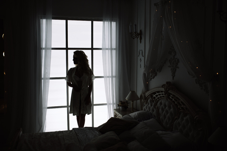 Silhouette of a fashion woman by the window. Wonderful portrait of a girl in a beautiful silk dressing gown.の写真素材