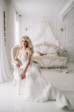 Wedding. Bride in a beautiful dress indoors in a white studio, like at home. The fashionable wedding style is taken in full length. Young attractive blond model with curly hair, like a brideの写真素材